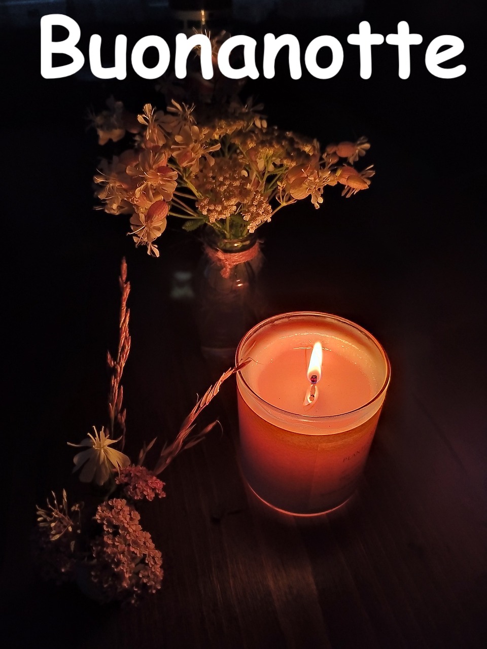 una romanticissima candela arancionerossa illumina un vaso con fiori notturni 